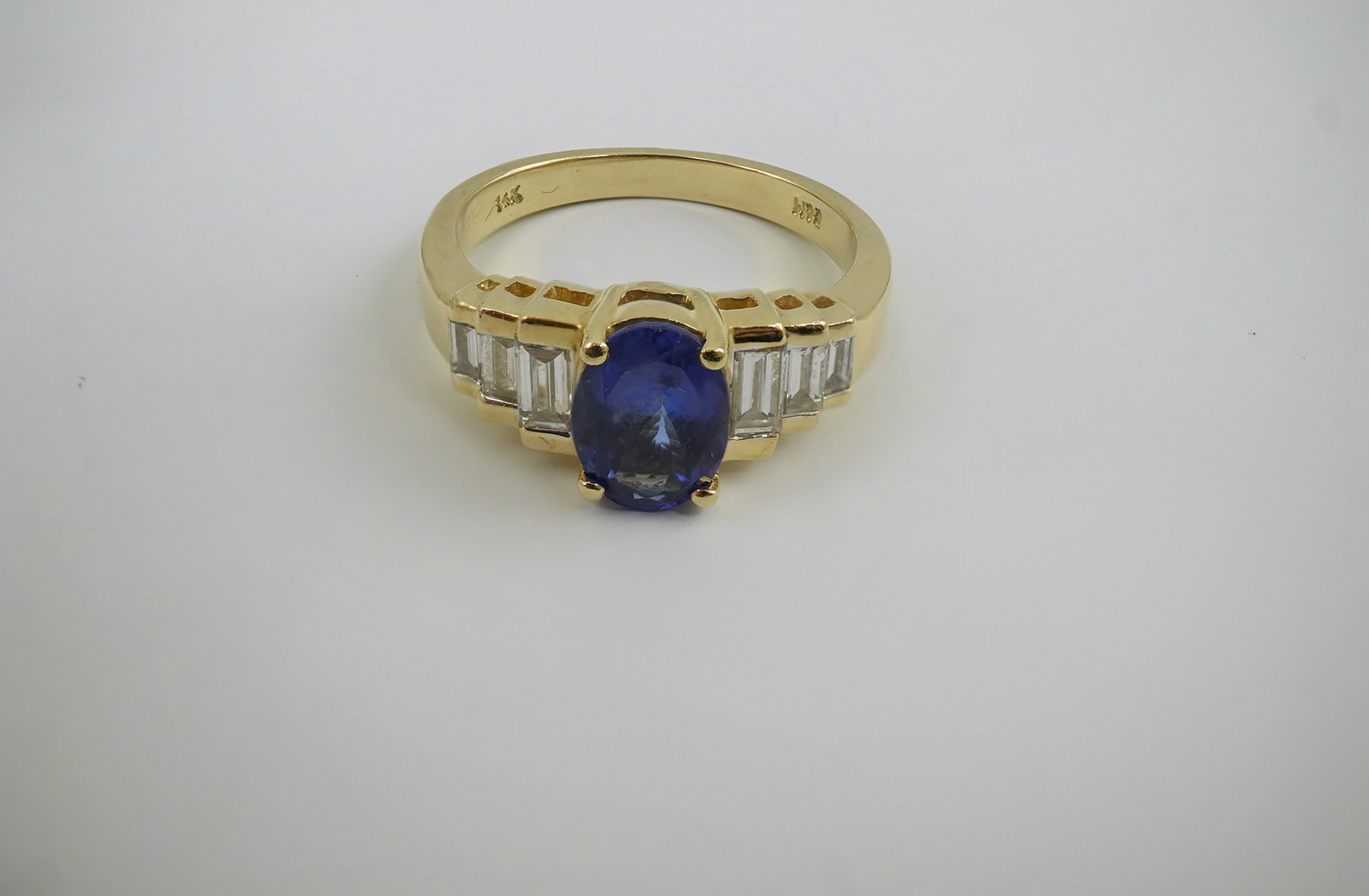 A modern 14k gold and single stone oval cut tanzanite set dress ring, with six stone graduated baguette cut diamond set shoulders